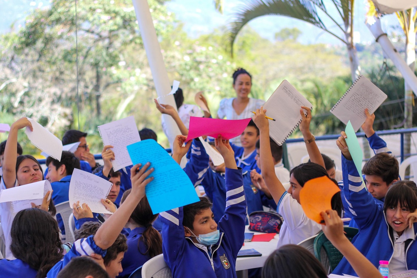 Niños y niñas con uniforme levantan al aire las hojas con sus textos durante un taller al aire libre
