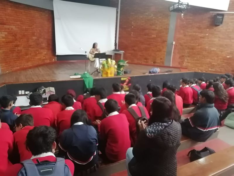Estudiantes con uniforme en un auditorio escuchando a una poeta en el escenario